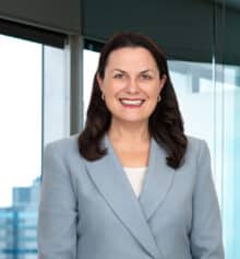 Professional headshot of Jennifer M. Horn, construction lawyer and founding partner, smiling and wearing a light blue blazer over a white top, posed in front of an office window overlooking Philadelphia.