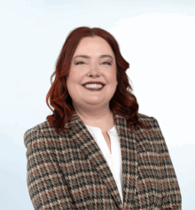 Professional headshot of Kathryne Hemmings, a Philadelphia construction defect attorney. She is smiling, with long wavy auburn hair, wearing a white blouse and a patterned houndstooth blazer, posed against a light blue background.