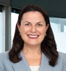 Professional headshot of Jennifer M. Horn, construction lawyer and founding partner, smiling and wearing a light blue blazer over a white top, posed in front of an office window overlooking Philadelphia.