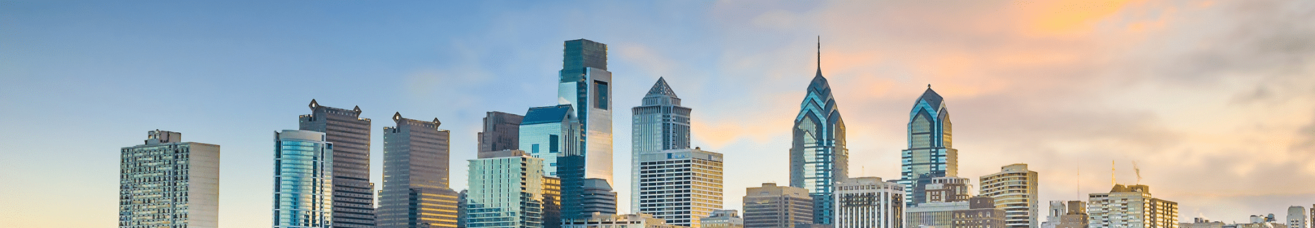Philadelphia skyline at sunset, with Center City buildings reflected in the Schuylkill River and Interstate 76 along the riverbank.